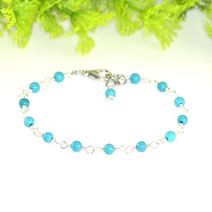 May include: A delicate silver chain bracelet with turquoise blue beads. The bracelet has a lobster clasp closure.