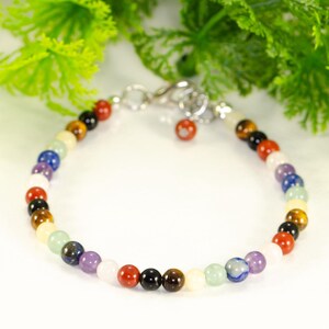 May include: A multi-coloured gemstone bracelet with a silver clasp. The bracelet is made up of various beads in shades of red, black, brown, yellow, green, blue, purple, and white. The text "Shokh Jewelry" is visible in the top right corner.