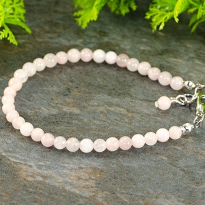 May include: A delicate pink rose quartz bracelet with a silver clasp. The bracelet is made of small, round beads and is strung on a clear elastic cord.