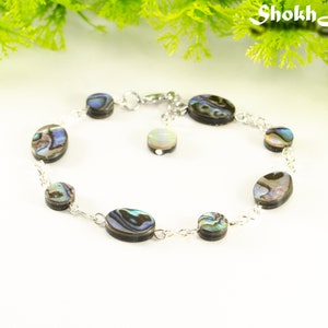 May include: A silver chain bracelet featuring oval-shaped abalone shell beads. The beads have a dark brown base with iridescent blue, green, and purple hues.