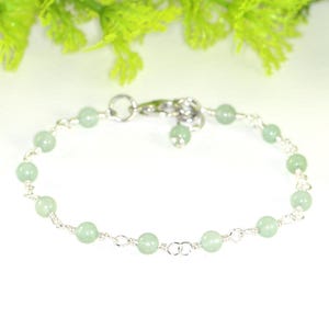May include: A delicate silver chain bracelet with light green beads. The bracelet has a lobster clasp closure.