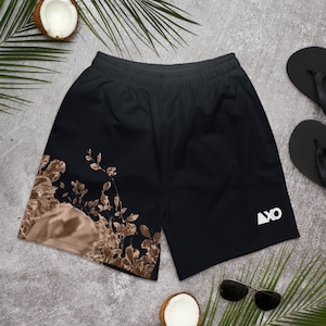 Op de afbeelding: Zwarte sportshort met een elastische tailleband en een wit logo op de rechterpijp. De linkerpijp heeft een bruine en beige botanische print van bladeren en takken. De short is gemaakt van een effen zwarte stof.