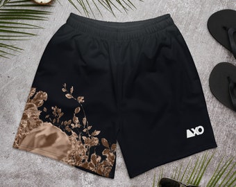May include: Black athletic shorts featuring an elastic waistband and a white logo on the right leg. The left leg displays a brown and tan botanical print of leaves and branches. The shorts are constructed from a solid black fabric throughout.