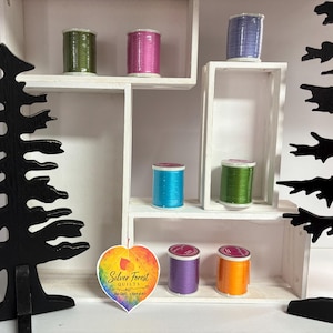 May include: Seven spools of colorful sewing thread in shades of olive green, magenta, lavender, bright blue, lime green, purple, and orange. A heart-shaped tag with the text Silver Forest QUILTS and Your Quilt, A Work of Art is included.