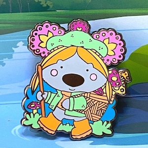 May include: A colorful enamel pin featuring a cartoon animal with a flower crown, wearing a green jacket and holding a stick. The animal has a blue and yellow striped scarf and is wearing orange boots.