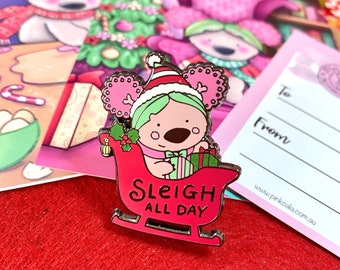 Può includere: Un koala rosa e verde con un cappello da Babbo Natale cavalca una slitta rossa con il testo "Sleigh All Day".