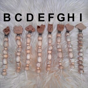 May include: Nine wooden baby teethers with different animal and vehicle designs. Each teether has a wooden clip and is strung with wooden beads.