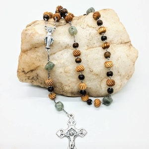 May include: A wooden rosary with green and brown beads, a silver crucifix, and a silver charm of the Virgin Mary.