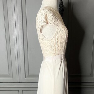 Op de afbeelding: Een wit kant topje met een witte rok. De rok is lang en zwierig. Het topje heeft korte mouwen en een ronde hals. De outfit is op een wit mannequin.