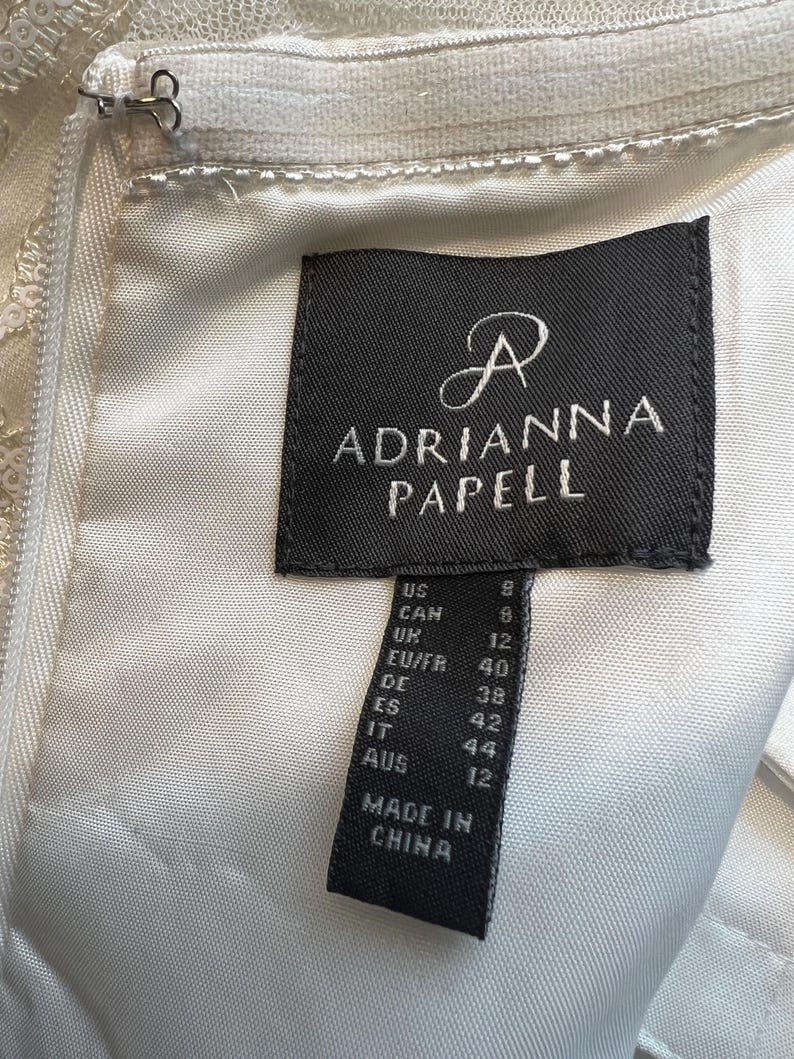 May include: A black and white size tag with the text "Adrianna Papell" and size conversions for US, Canada, UK, EU/FR, DE, ES, IT, and AUS. The tag also says "Made in China."