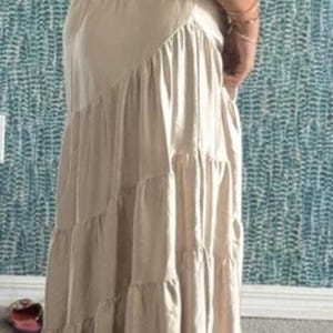 May include: A beige maxi dress with a tiered skirt and puffed sleeves. The dress has a fitted bodice and a flowing, floor-length skirt. The fabric appears to be a lightweight material, suitable for warmer weather.