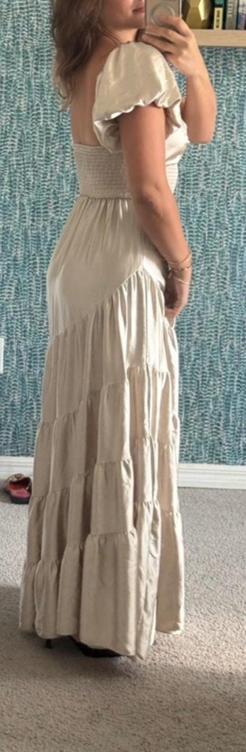 May include: A beige maxi dress with a tiered skirt and puffed sleeves. The dress has a fitted bodice and a flowing, floor-length skirt. The fabric appears to be a lightweight material, suitable for warmer weather.