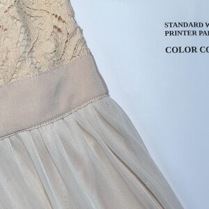 May include: Close-up of a formal dress featuring a cream-colored lace bodice and a flowing, light beige skirt. A decorative band with sparkling embellishments accents the waist. The text "STANDARD WHITE PRINTER PAPER for COLOR COMPARISON" is visible.