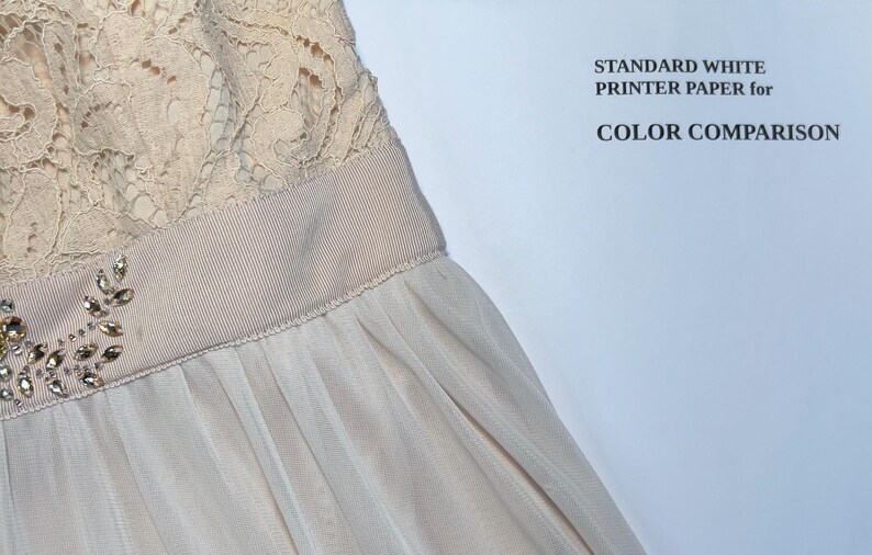 May include: Close-up of a formal dress featuring a cream-colored lace bodice and a flowing, light beige skirt. A decorative band with sparkling embellishments accents the waist. The text "STANDARD WHITE PRINTER PAPER for COLOR COMPARISON" is visible.