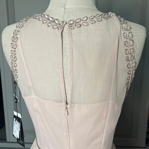 Puede incluir: Vestido de fiesta rosa claro sobre un maniqu&iacute;. El vestido presenta un escote y tirantes con cuentas, con un cintur&oacute;n de cuentas a juego en la cintura. La espalda tiene un panel transparente y cierre de cremallera.