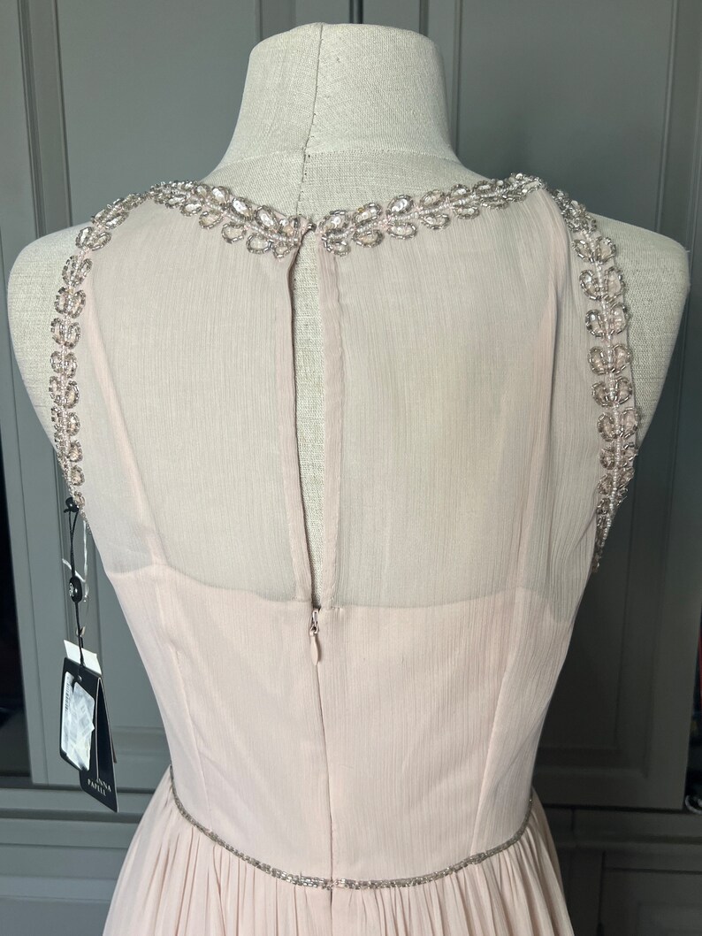 Puede incluir: Vestido de fiesta rosa claro sobre un maniqu&iacute;. El vestido presenta un escote y tirantes con cuentas, con un cintur&oacute;n de cuentas a juego en la cintura. La espalda tiene un panel transparente y cierre de cremallera.