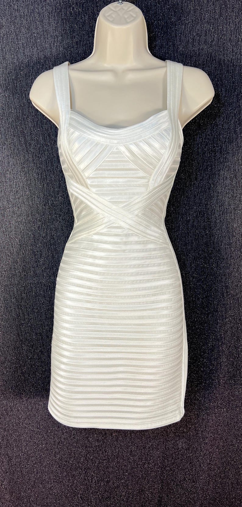 May include: White, bodycon dress with a structured bodice and a fitted skirt. The dress features a scoop neckline, thick straps, and horizontal ribbing throughout the design. The dress is displayed on a mannequin.