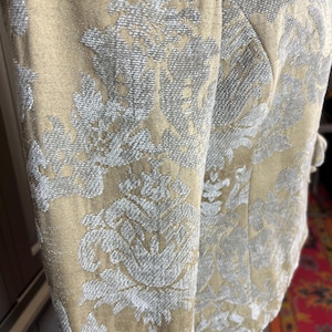 May include: Close-up of a beige jacket with a floral pattern in silver. The jacket has a tailored fit with a structured design. The fabric has a textured appearance, and the sleeves are visible.