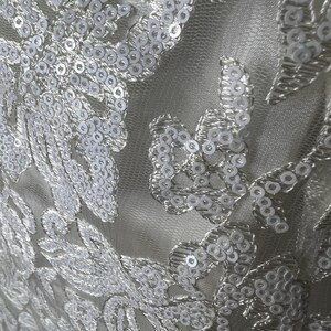 May include: White fabric with a delicate floral pattern embellished with white sequins.