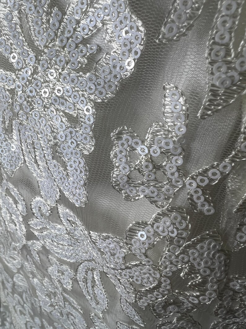 May include: White fabric with a delicate floral pattern embellished with white sequins.