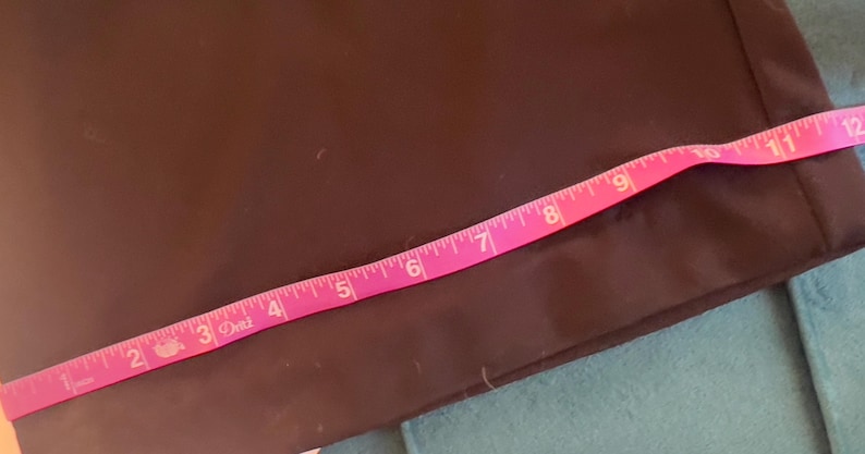 Puede incluir: Una tela marr&oacute;n oscuro con una cinta m&eacute;trica rosa colocada encima. La cinta muestra medidas de 2,5 a 30,5 cm. La tela parece ser una prenda de vestir o un art&iacute;culo similar.
