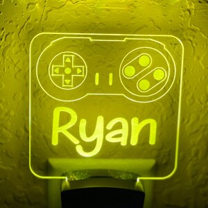 May include: A yellow night light shaped like a video game controller with the name "Ryan" written below it.
