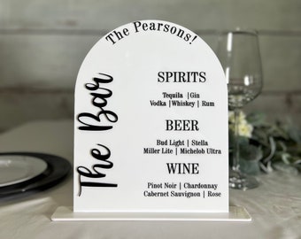 May include: White acrylic sign with a black arch shape at the top. The sign says "The Pearsons!" and lists the drinks available: "Spirits", "Tequila | Gin | Vodka | Whiskey | Rum", "Beer", "Bud Light | Stella | Miller Lite | Michelob Ultra", "Wine", "Pinot Noir | Chardonnay | Cabernet Sauvignon | Rose".