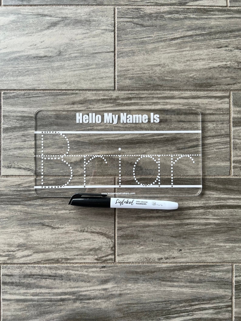 Pode incluir: Um quadro branco de pl&aacute;stico transparente com o texto "Hello My Name Is" e um contorno pontilhado da palavra "Brian". Um marcador de quadro branco preto est&aacute; deitado ao lado do quadro.