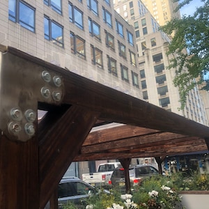 Pode incluir: Uma p&eacute;rgola de madeira com um suporte de metal fixado com v&aacute;rios parafusos. A p&eacute;rgola &eacute; feita de madeira marrom escura e est&aacute; presa a um pr&eacute;dio com grandes janelas.