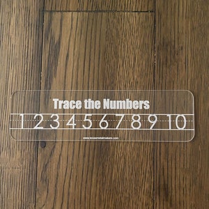 Op de afbeelding: Een transparante acryl traceergids met de tekst "Trace the Numbers" en de cijfers 1 tot en met 10. Het bevat traceerlijnen en het websiteadres www.texasmetalmakers.com.