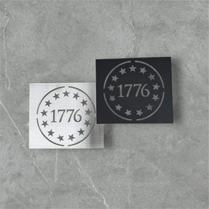 May include: Two white and black square signs with a circle design featuring a ring of stars and the number 1776 in the center.