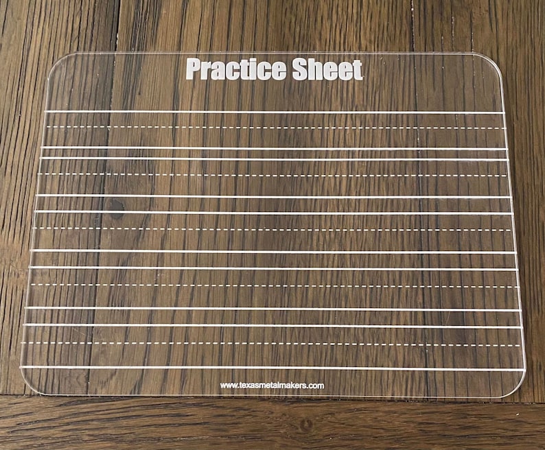 Op de afbeelding: Een heldere acryl oefenvel met witte gedrukte lijnen en de woorden "Practice Sheet" bovenaan. Het vel heeft afgeronde hoeken en is ontworpen voor het oefenen van handschrift. De website www.texasmetalmakers.com is onderaan afgedrukt.