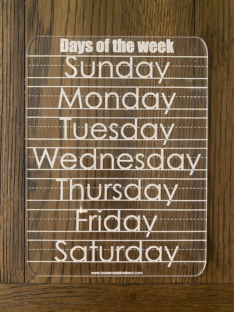 Op de afbeelding: Transparant acryl leerbord voor de dagen van de week met witte letters. De woorden "Days of the week" staan bovenaan, gevolgd door de dagen van de week. Stippellijnen zijn inbegrepen voor schrijfoefeningen. De website www.texasmetalmakers.com staat onderaan.