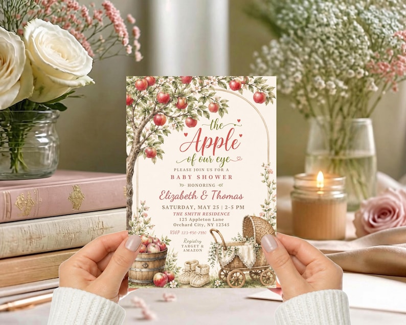 May include: A rectangular baby shower invitation card featuring a watercolour illustration of an apple tree, a wooden barrel filled with apples, and a vintage wicker baby carriage. The text reads: the Apple of our eye, Elizabeth & Thomas.