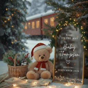 Puede incluir: Un oso de peluche con gorro y bufanda de Papá Noel junto a un letrero que dice "Bebé Thompson llega en septiembre de 2026". Una cesta de vegetación y un tren al fondo, con luces navideñas.