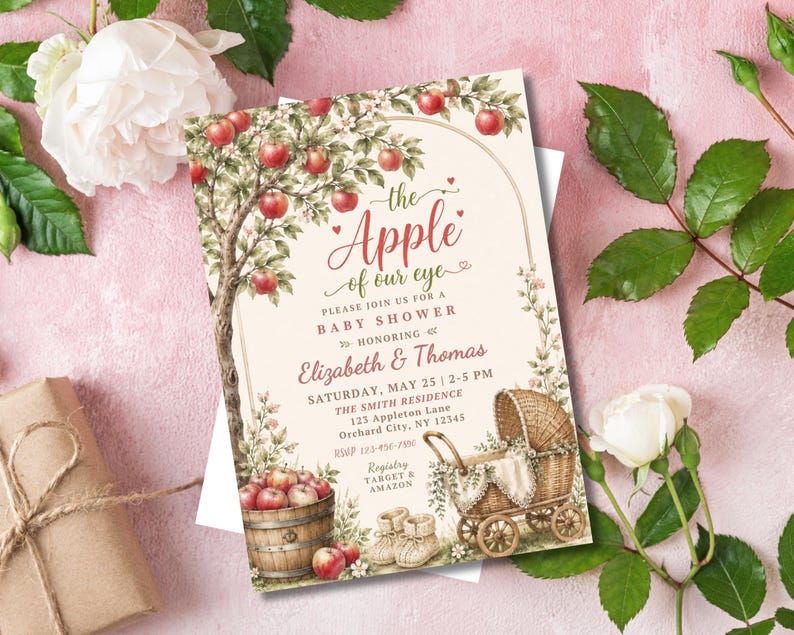 May include: A rectangular baby shower invitation card featuring a watercolour illustration of an apple tree, a wooden barrel filled with red apples, and a wicker baby carriage. The text reads: the Apple of our eye, PLEASE JOIN US FOR A BABY SHOWER, HONORING Elizabeth & Thomas, SATURDAY, MAY 25 | 2-5 PM, THE SMITH RESIDENCE, 123 Appleton Lane, Orchard City, NY 12345, RSVP 123-456-7890, Registry TARGET & AMAZON.