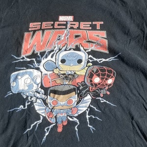 Puede incluir: Camiseta negra con un gráfico de personajes de Marvel Secret Wars en estilo Pop! Los personajes incluyen al Capitán América, Spider-Man, Iron Man y otros.