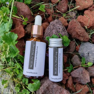 May include: Two amber glass bottles with gold lids and white labels. The labels read "MidLife Healing a tincture for your mind, body, & soul" and "Spiritual Boundaries".