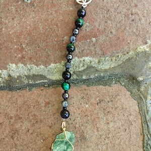 May include: A black and green beaded necklace with a silver pentagram charm and a green crystal pendant.