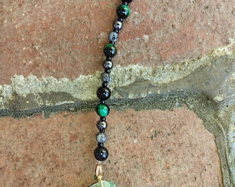 May include: A black and green beaded necklace with a silver pentagram charm and a green crystal pendant.