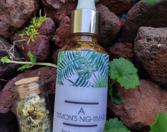 May include: A glass bottle with a silver cap and a white dropper. The bottle is filled with a brown liquid and has a white label with the text "A DEMON'S NIGHTMARE Spiritual Boundaries".