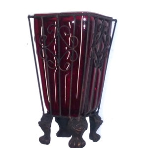 May include: A red glass vase with a metal cage and three decorative feet.