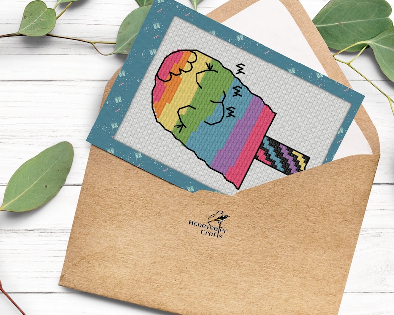May include: A colorful rainbow-colored popsicle with a black and white striped stick. The popsicle is on a blue card with a white background and the text "Honeyweaver Crafts".
