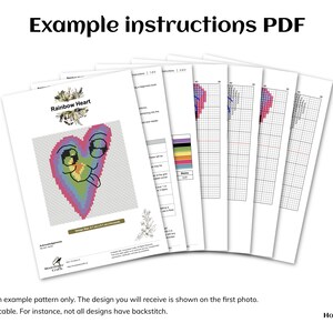 May include: A cross-stitch pattern for a rainbow heart with a smiling face and a tongue sticking out. The pattern is on a white sheet of paper with the title "Rainbow Heart" at the top. The pattern is part of a set of instructions for a cross-stitch project.