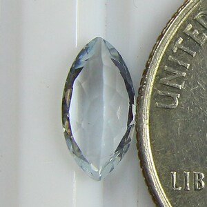 May include: A light blue marquise-shaped gemstone with a faceted cut. The gemstone is about the size of a US dime.