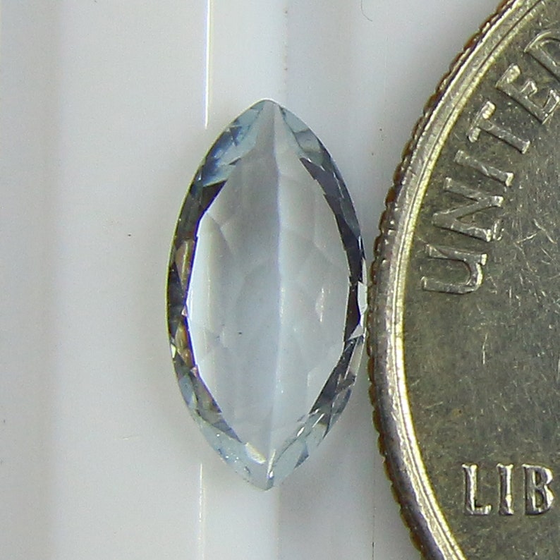 May include: A light blue marquise-shaped gemstone with a faceted cut. The gemstone is about the size of a US dime.
