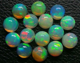 May include: A collection of 14 round, iridescent opal cabochons. The opals are a pale white with flashes of green, blue, and orange.