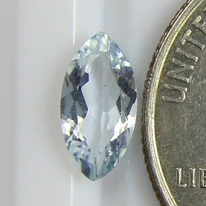 May include: A light blue marquise-shaped aquamarine gemstone, approximately 6mm in length, next to a US quarter for size comparison.