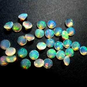 May include: A collection of 20 round, iridescent opal gemstones. The opals are a pale white color with flashes of green, blue, and yellow.