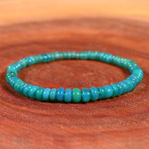 May include: A turquoise blue gemstone bracelet made of small, round beads. The bracelet is on a wooden surface.